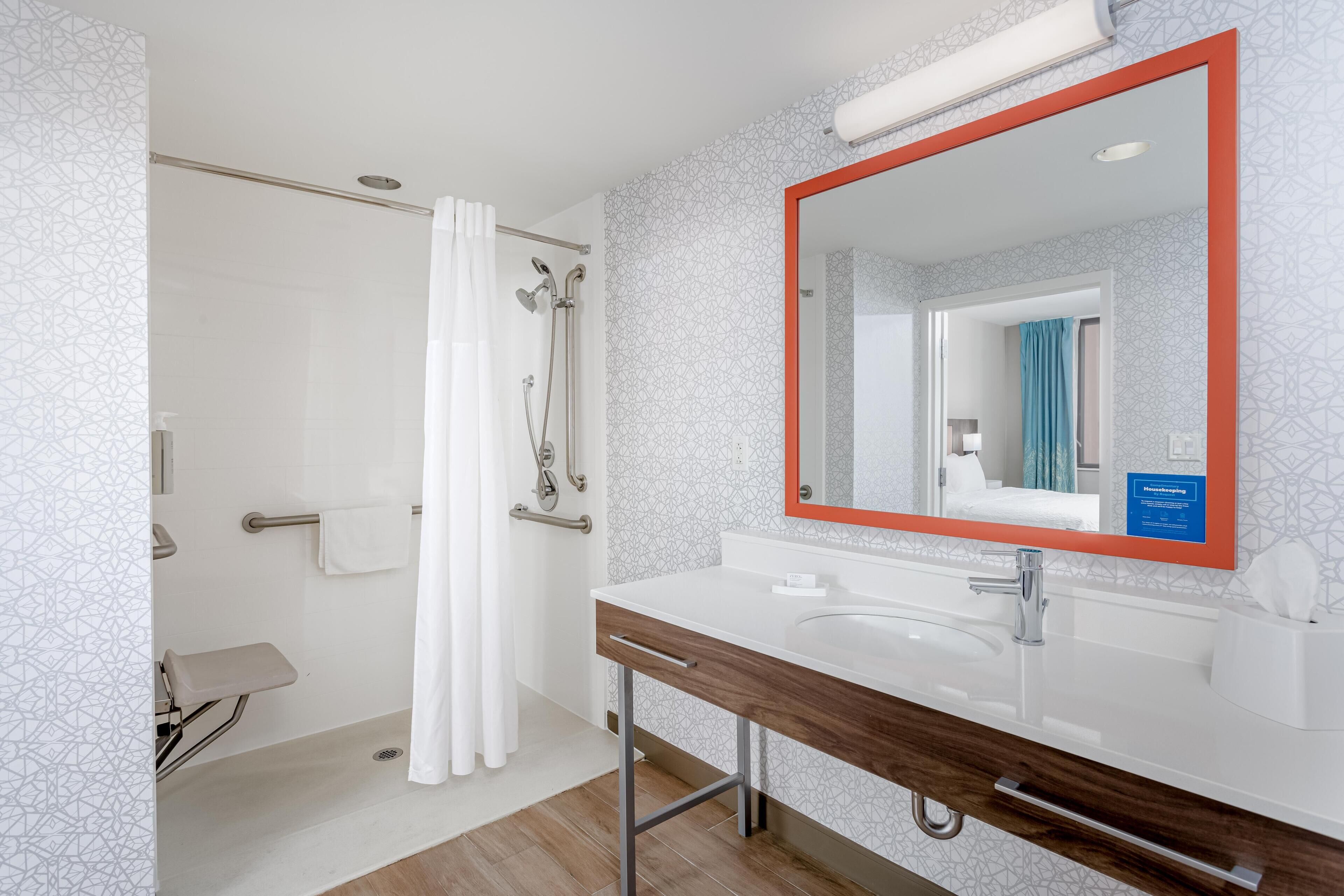Un bagno moderno con doccia, lavabo e specchio dalla cornice rossa.