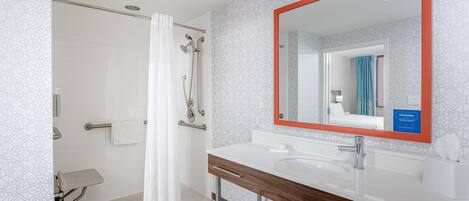 A modern bathroom with a shower, a sink, and a mirror with a red frame.