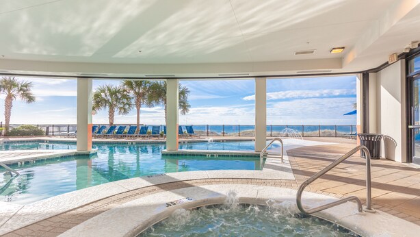 Uma área de piscina com hidromassagem, espreguiçadeiras e vista para o mar.