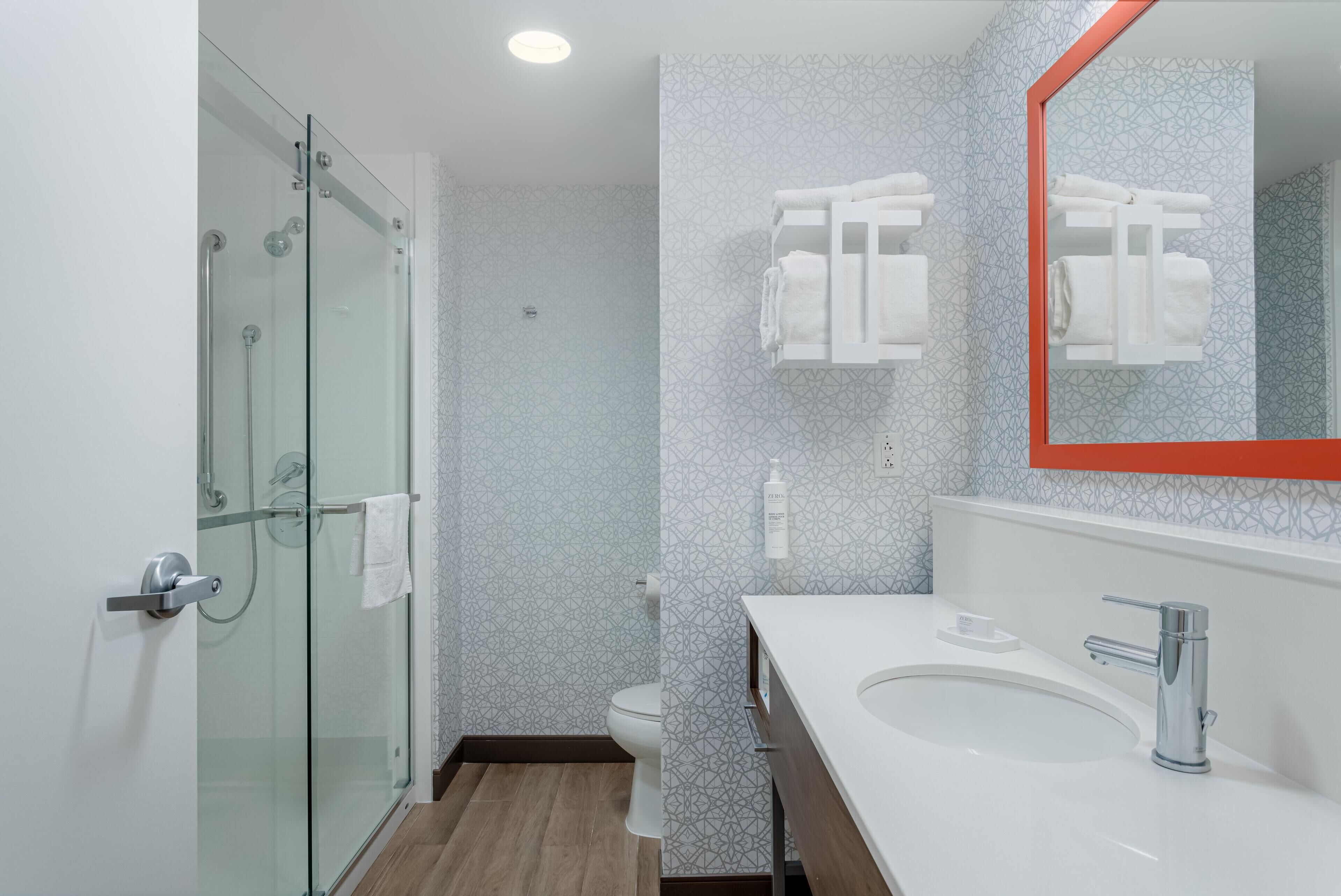 Ein modernes Badezimmer mit Duschkabine aus Glas, einem weißen Waschbecken mit Chromarmatur und einem an der Wand befestigten Handtuchhalter.