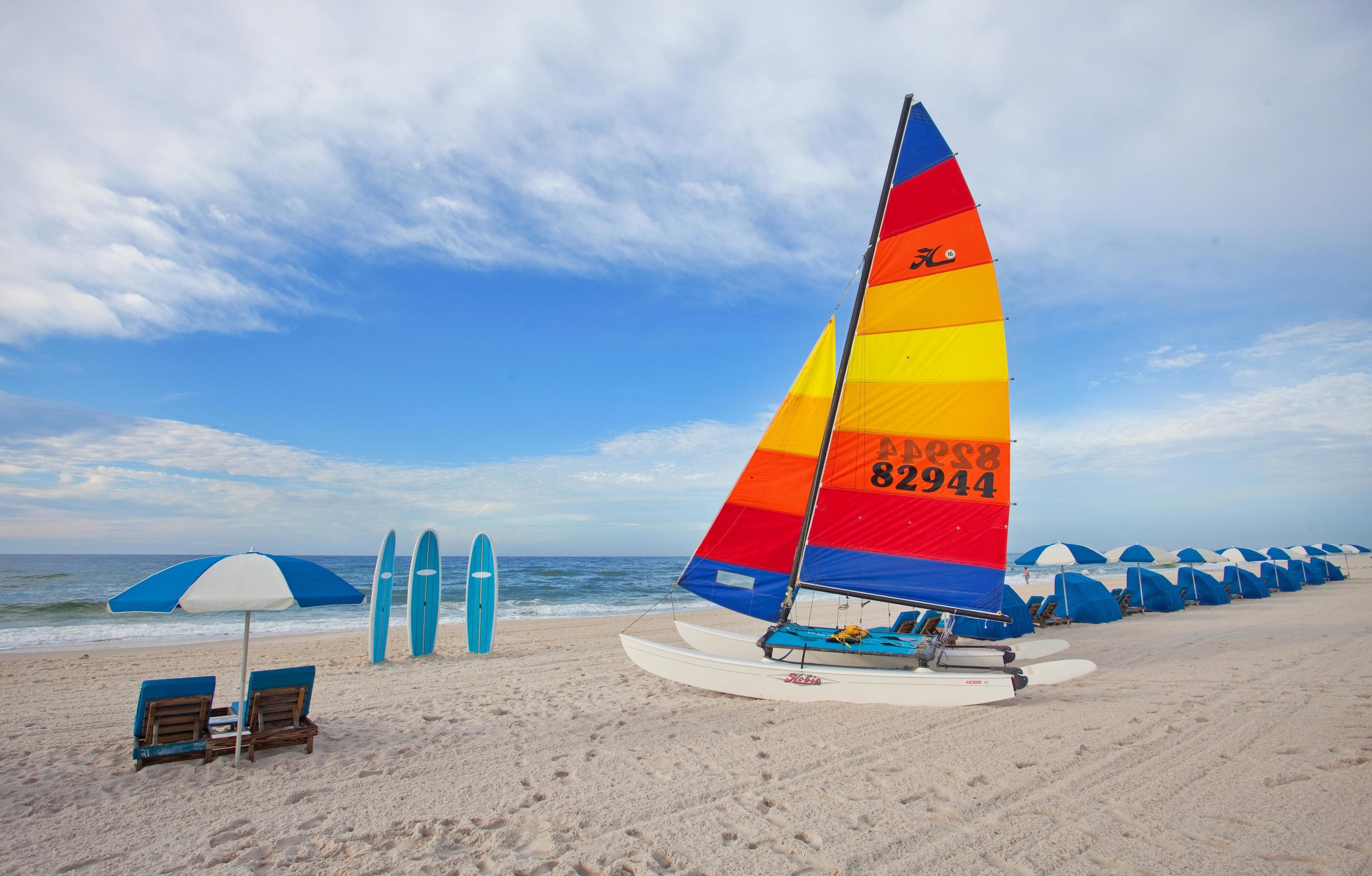 A beach with a colorful sailboat, beach chairs, and umbrellas.