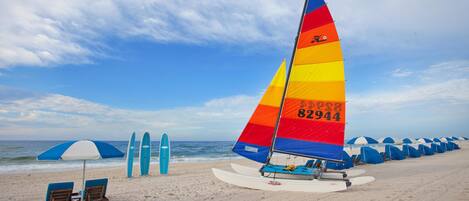 A beach with a colorful sailboat, beach chairs, and umbrellas.