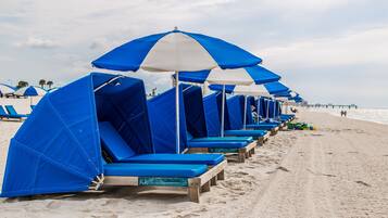 A row of beach chairs with blue and white umbrellas, arranged on a sandy beach.