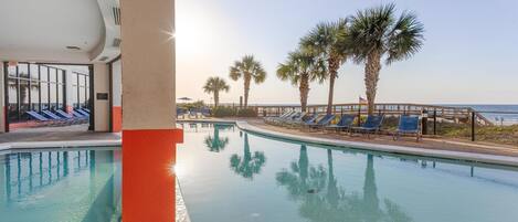 A pool area with clear water, blue lounge chairs, palm trees, and a view of the ocean.