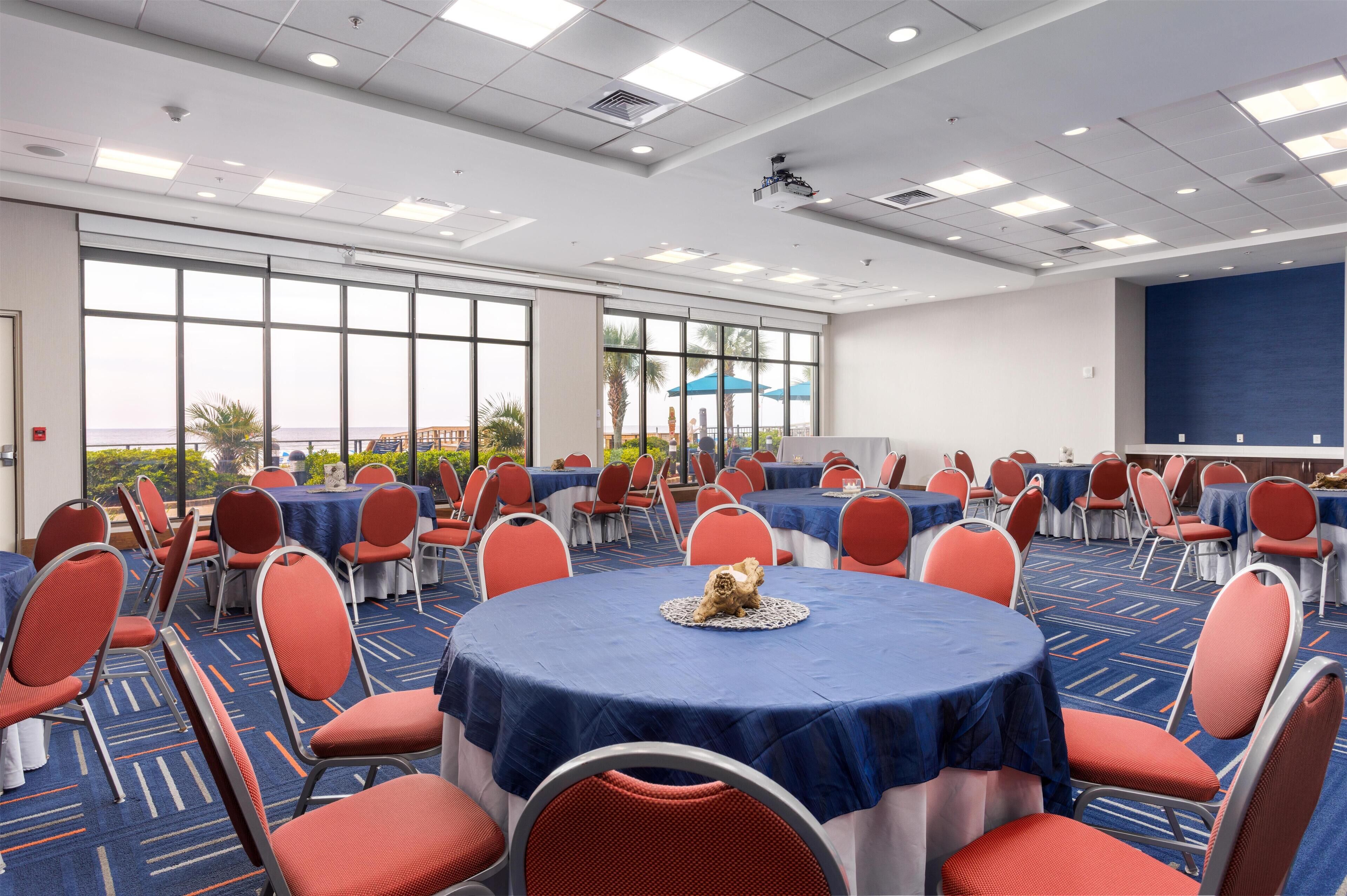 Une salle de conférence avec des tables rondes, des chaises rouges et un grand écran.