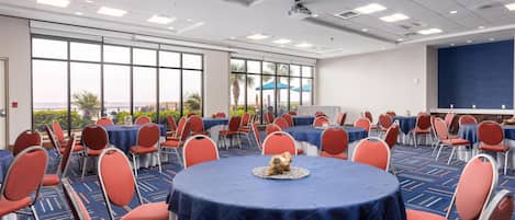 A conference room with round tables, red chairs, and a large screen.