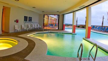 A swimming pool area with a hot tub, lounge chairs, and a view of the ocean.
