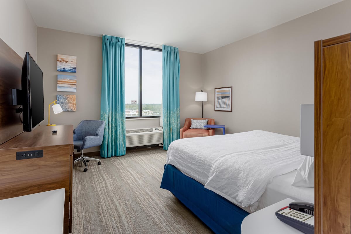 A hotel room with a bed, desk, chair, TV, and a window with curtains.
