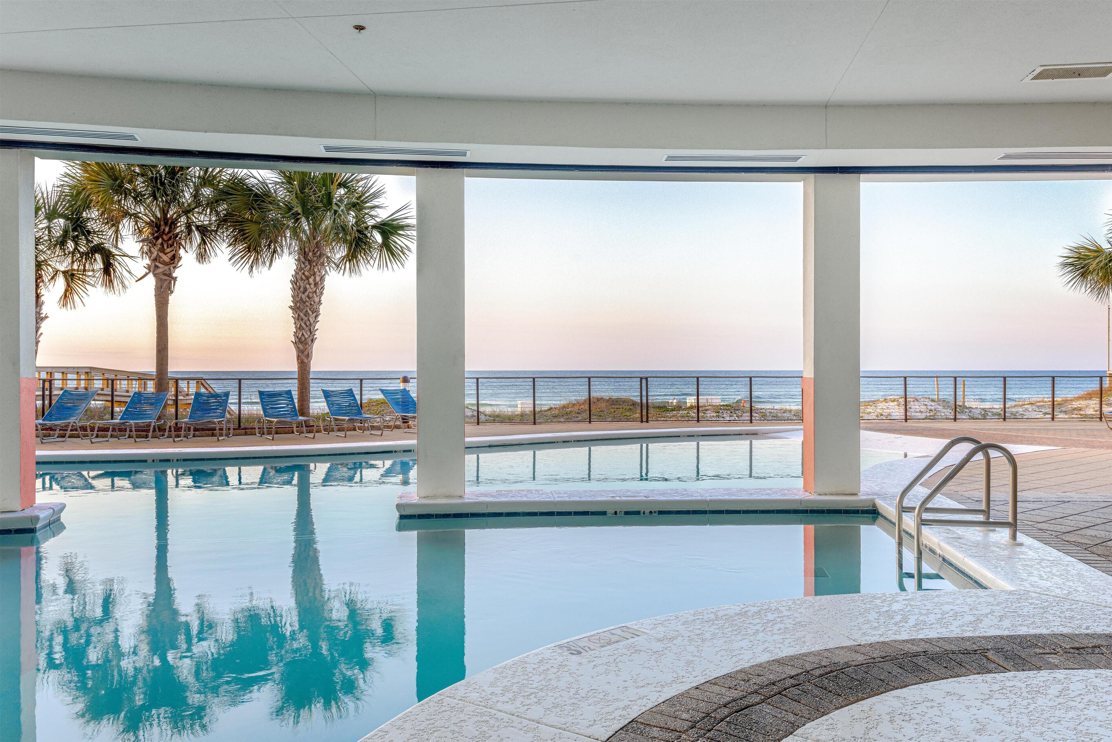 An indoor swimming pool with clear views of the beach and palm trees.