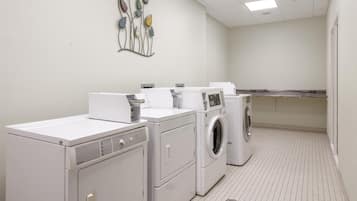 A laundry room with multiple washing machines and dryers, a tiled floor, and a decorative wall piece.