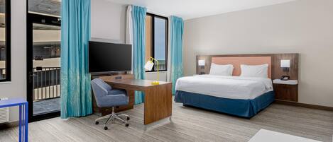 A hotel room with a bed, desk, chair, TV, and a balcony view.
