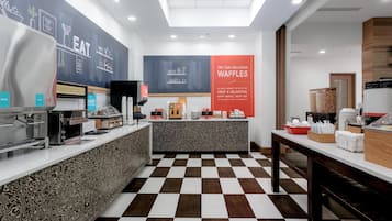 A modern breakfast area with a checkered floor, a counter with various food items, and a wall with a 'Breakfast Starts Here' sign.