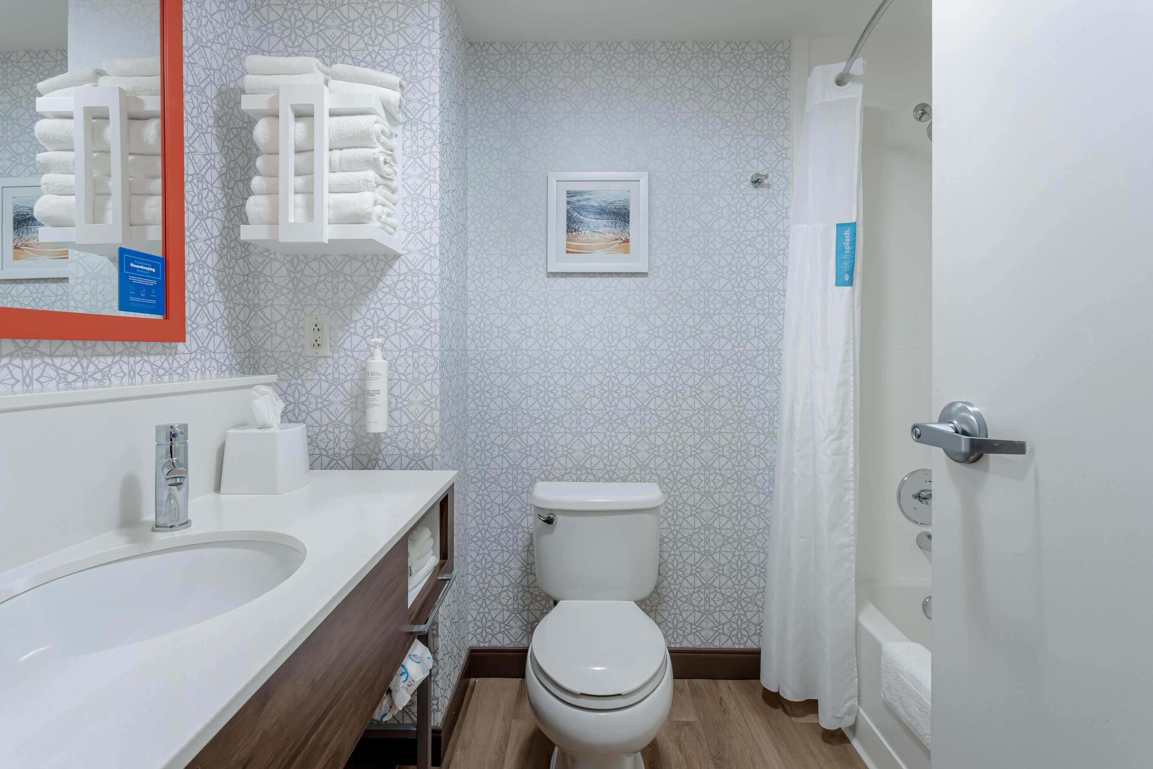 Ein modernes Badezimmer mit Waschbecken, Toilette und Duschbereich. An der Wand sind ein Handtuchhalter und ein gerahmtes Bild zu sehen.