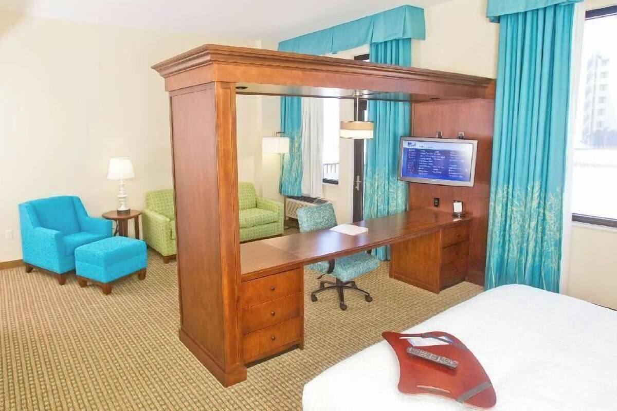 A hotel room with a wooden desk, a television, a bed, and two chairs.