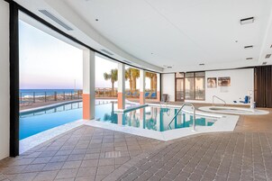 An indoor swimming pool with a view of the beach and palm trees.