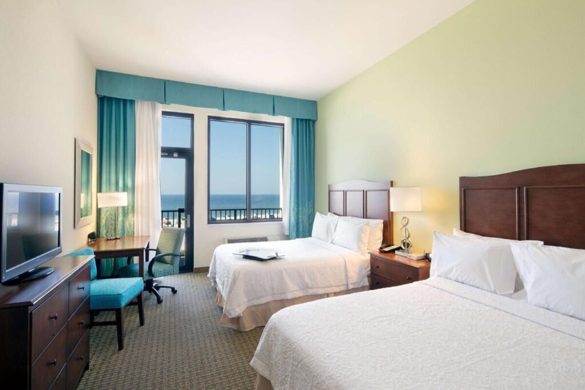 A hotel room with two beds, a desk with a TV, a chair, and a window with a view.