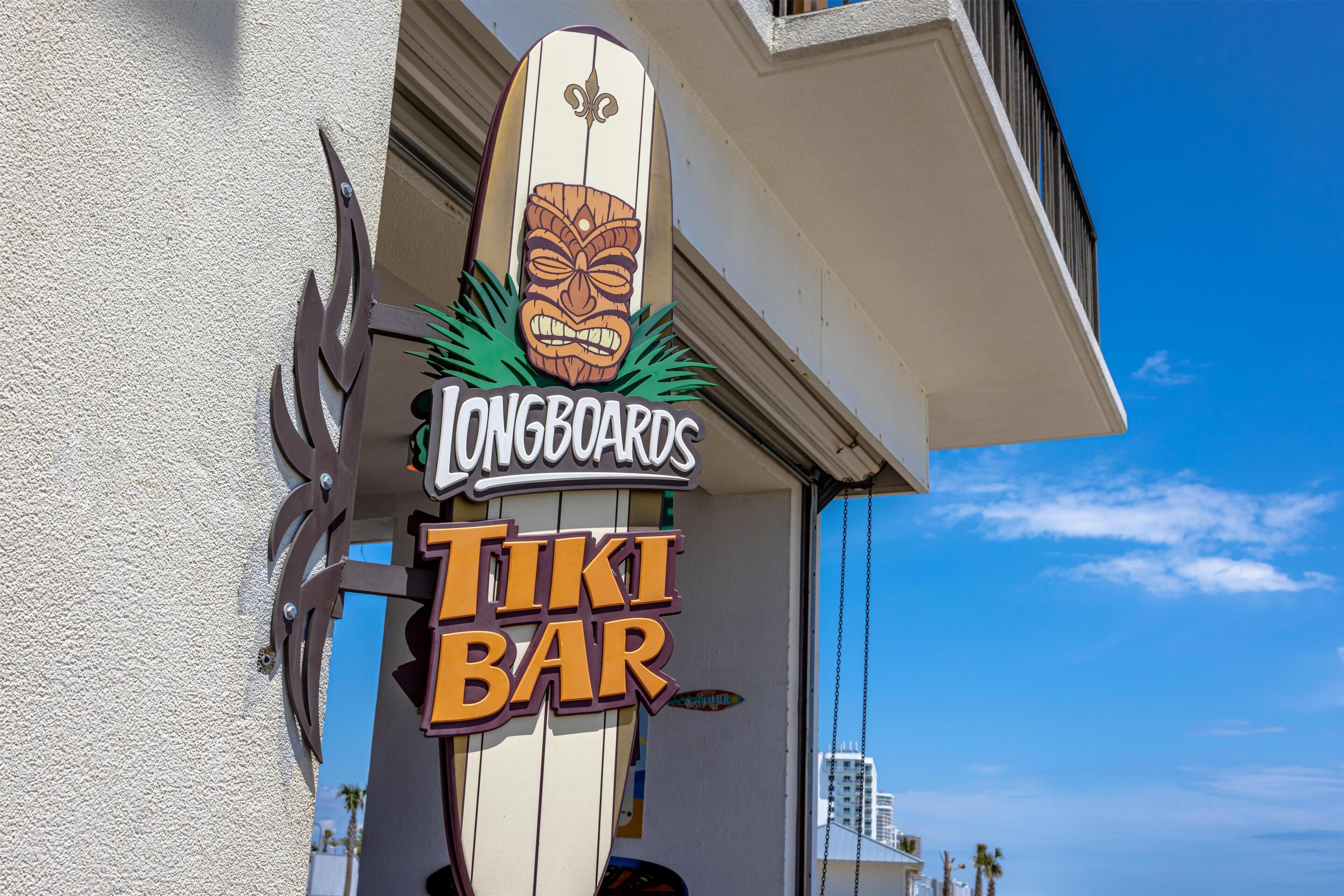 A tiki bar sign with a surfboard and a tiki mask design, indicating a beach-themed establishment.
