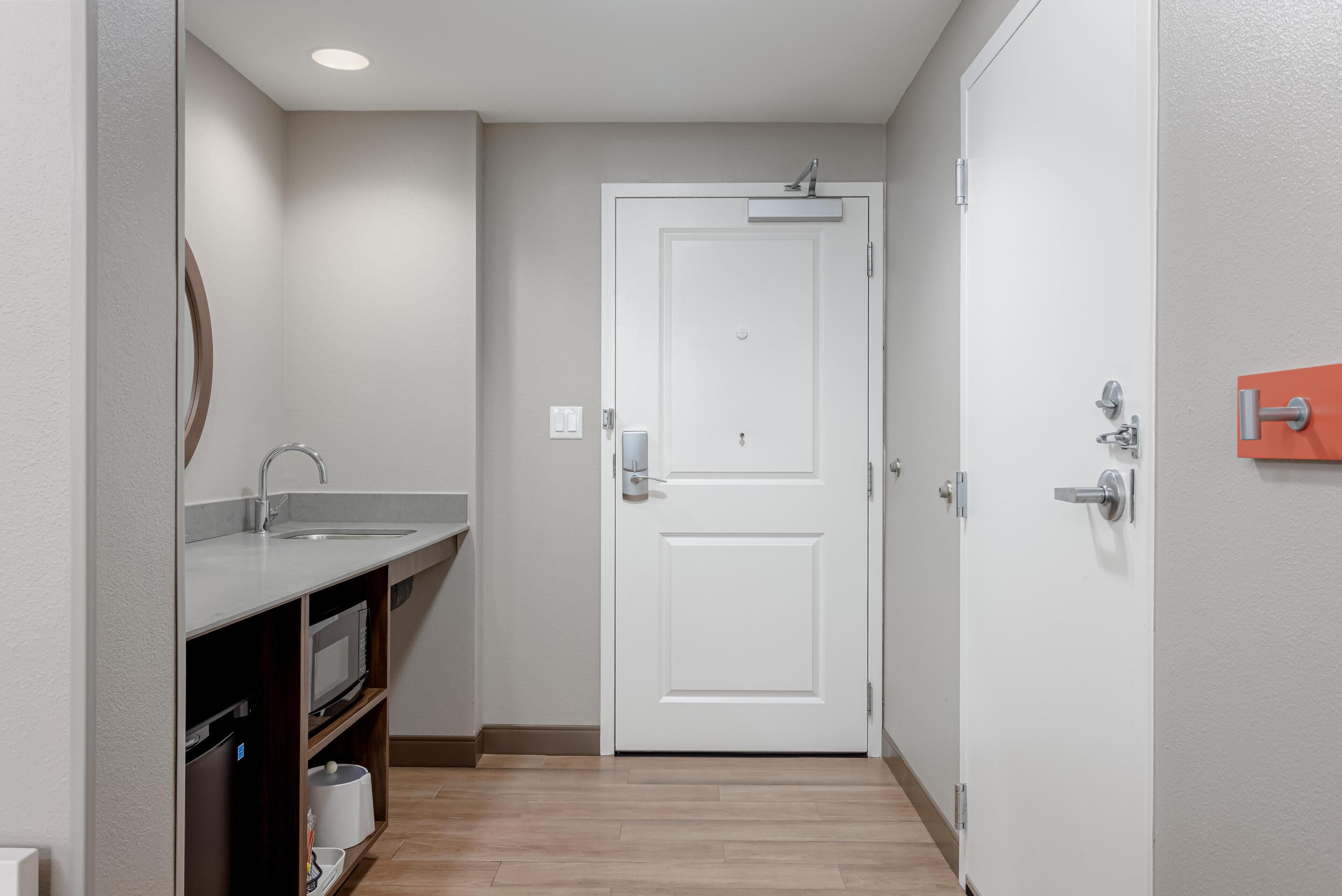 A narrow hallway with a white door, a sink, and a microwave.
