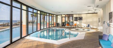 An indoor swimming pool with clear views of the ocean, a lounge area, and a no-lifeguard sign.