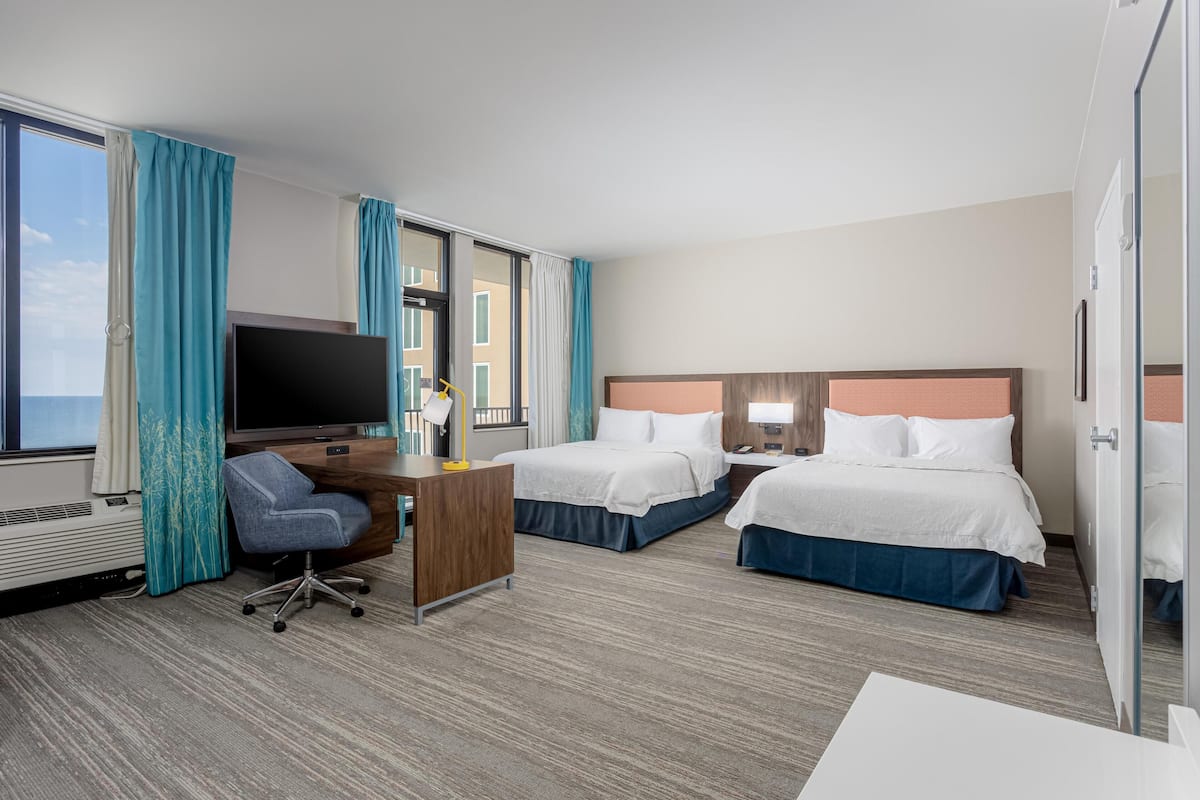 A hotel room with two beds, a desk with a computer, a TV, and a view of the ocean.