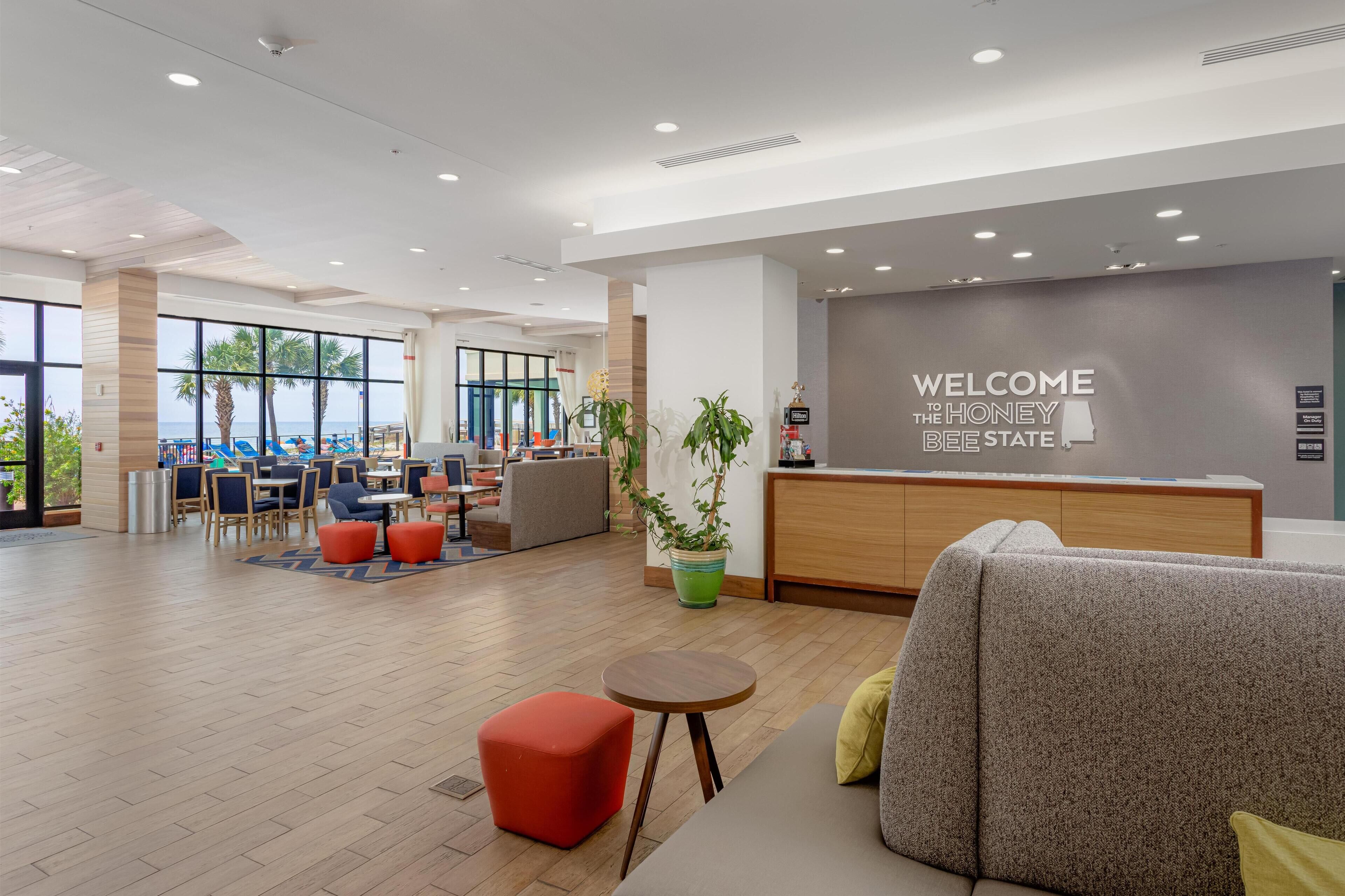 A modern hotel lobby with a reception desk, seating areas, and large windows offering views of the outdoors.