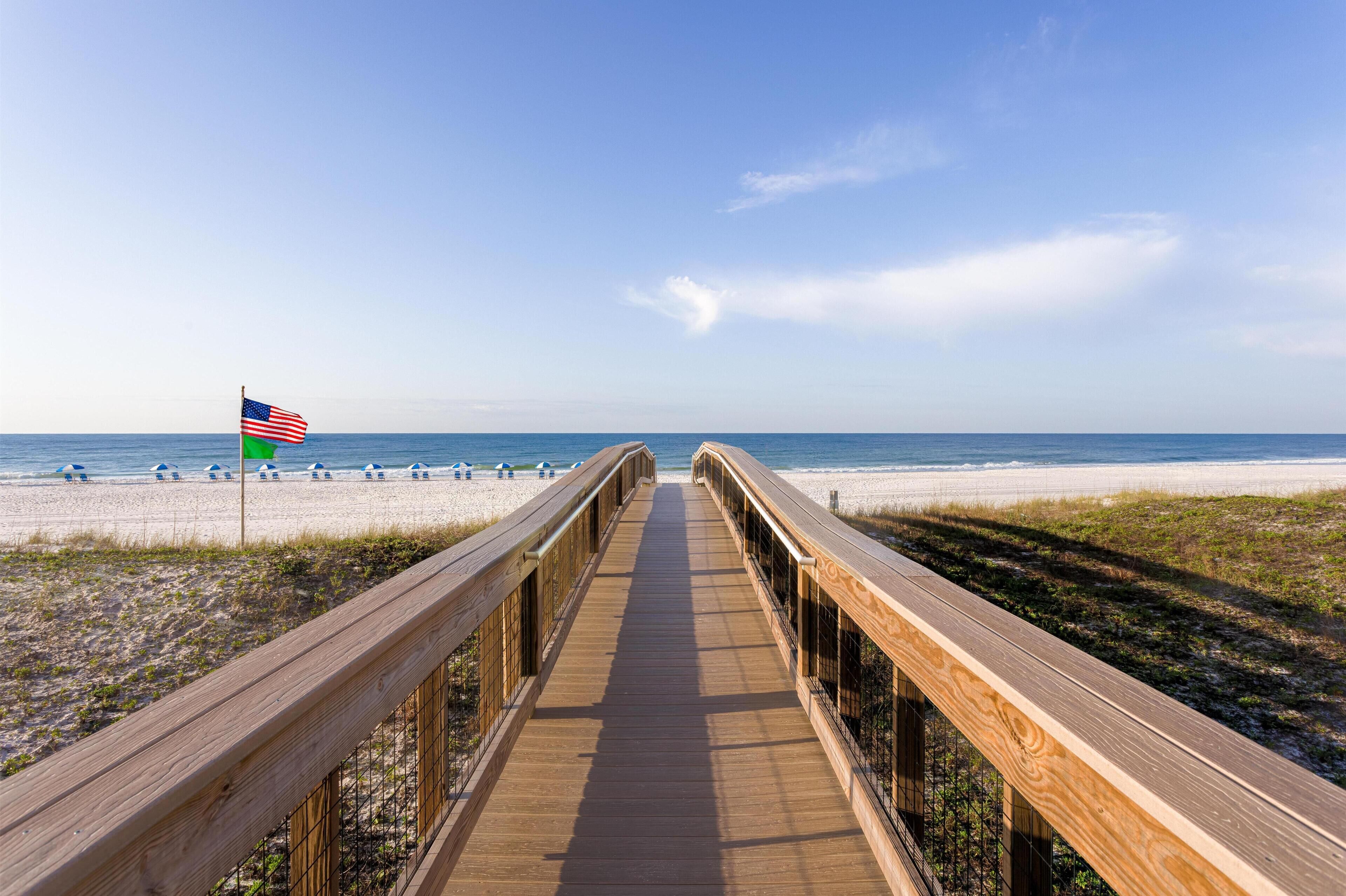 A wooden boardwalk leading to a beach with a flag.