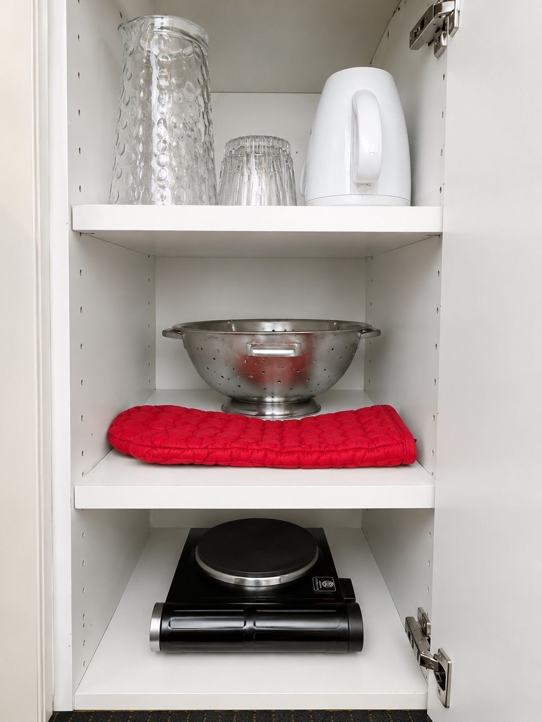 A kitchen with a colander, kettle, and a coffee maker on the shelf.