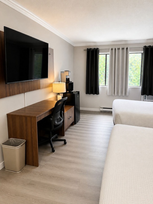 Habitación de hotel con cama, escritorio con computadora, televisor y ventana con cortinas.