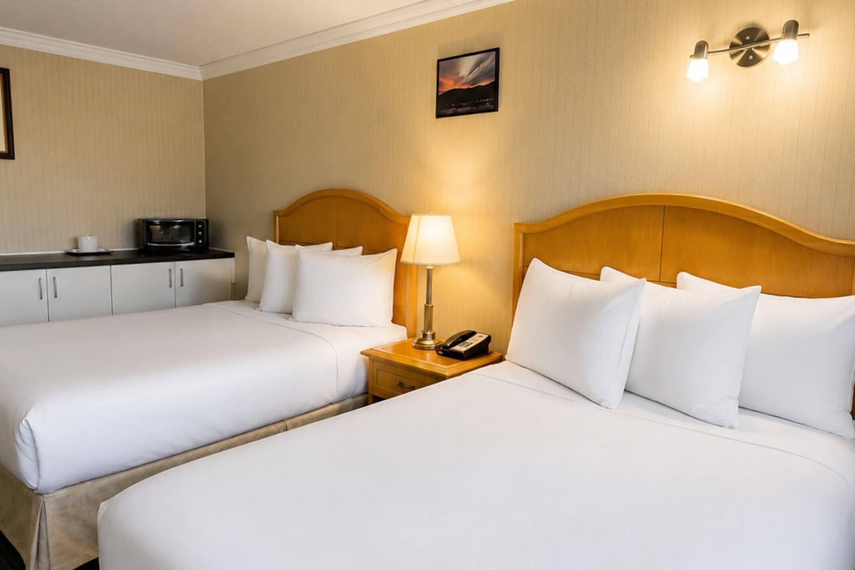 A hotel room with two beds, a microwave, a lamp, and a telephone on a bedside table.