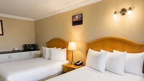 Una habitación de hotel con dos camas, una mesita de noche con lámpara, un microondas y un pequeño cuadro en la pared.