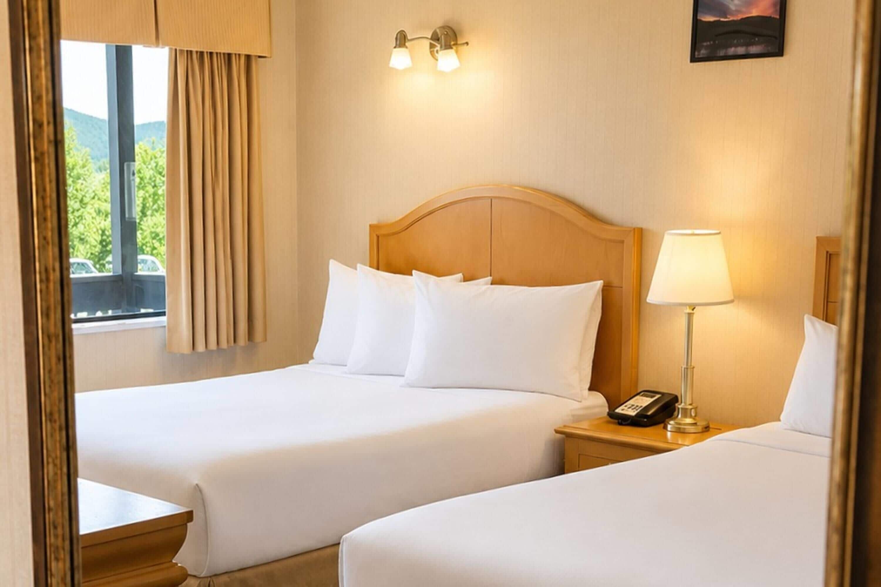 A hotel room with two beds, a nightstand with a lamp, and a window with curtains.