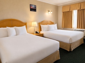 A hotel room with two beds, a nightstand with a lamp and phone, a wall-mounted light, and a window with curtains. - Travelodge by Wyndam Chetwynd (Chetwynd)