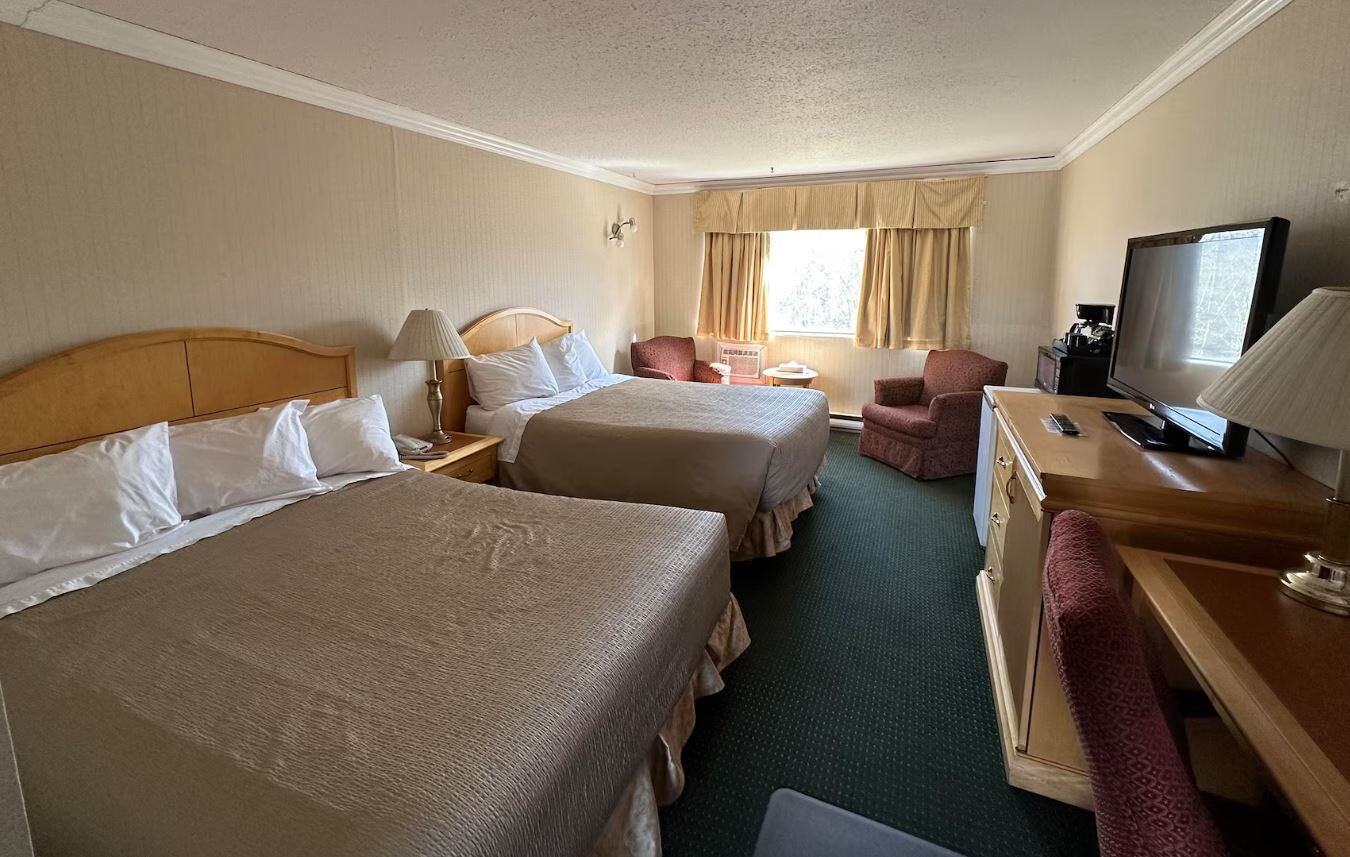 A hotel room with two beds, a desk, a TV, and a chair.