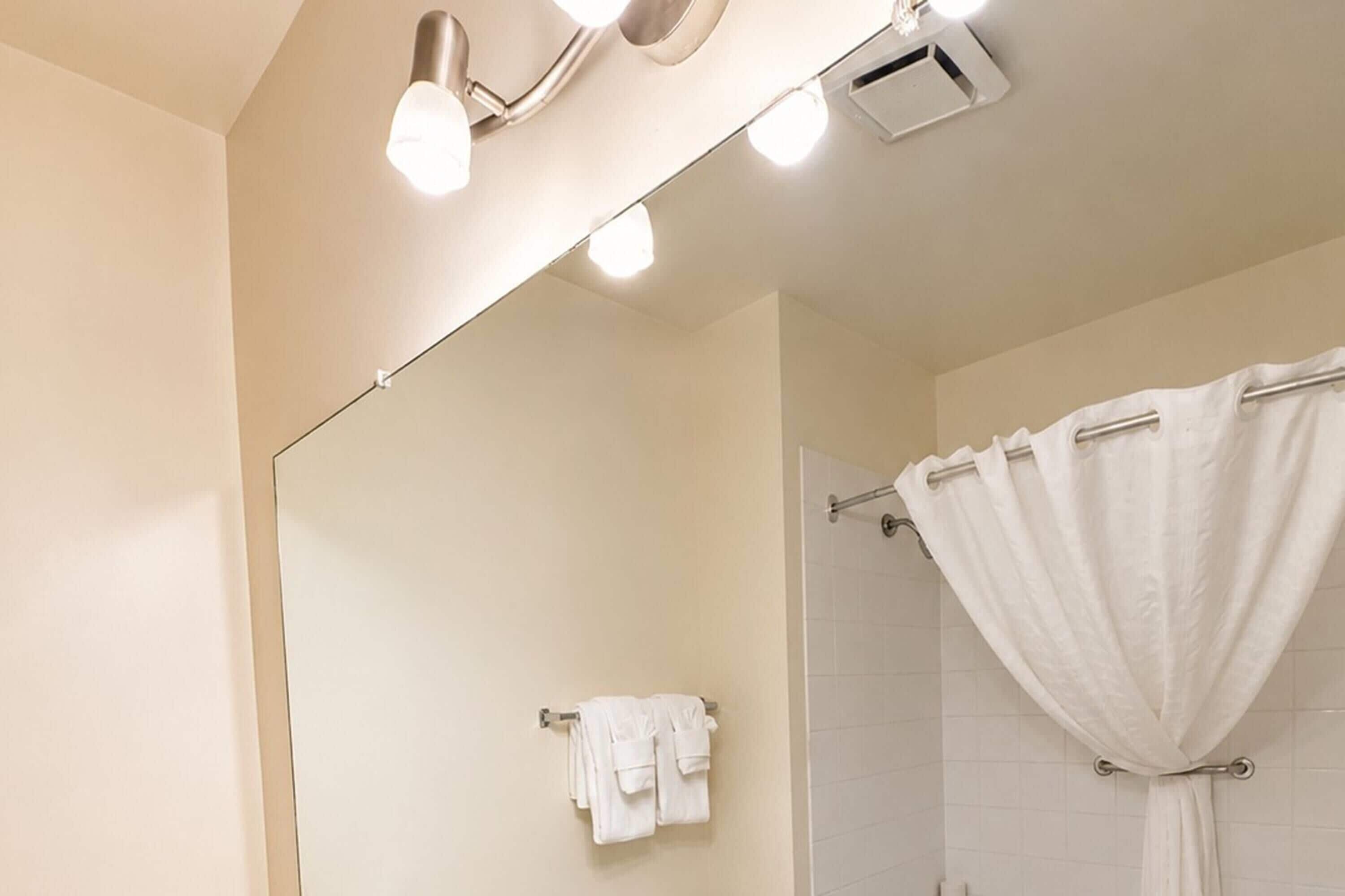 A bathroom with a large mirror, a towel rack with towels, and a shower curtain.