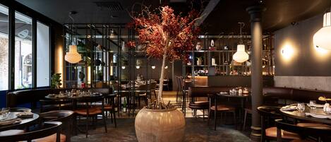A restaurant with round tables, chairs, and a large vase with a tree.
