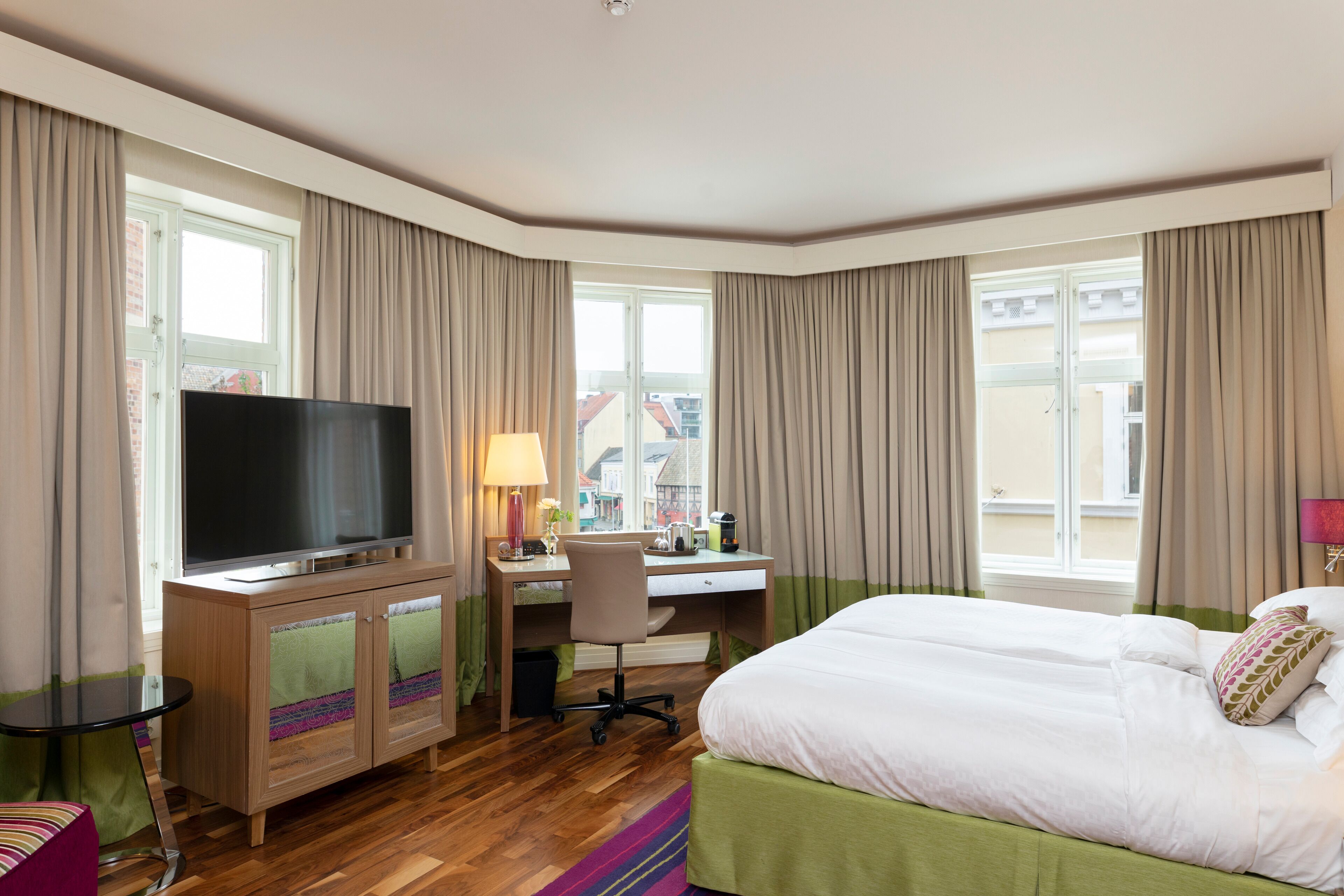 Habitación de hotel con cama, escritorio con computadora, televisor y ventana con cortinas.