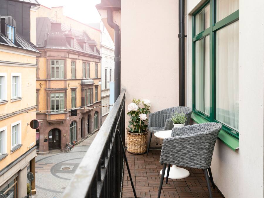 A balcony with wicker chairs and a table, overlooking a street with historic buildings.