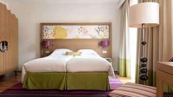 Una habitación de hotel con una cama, un cabecero con una obra de arte floral, una lámpara de noche y falda para la cama verde.