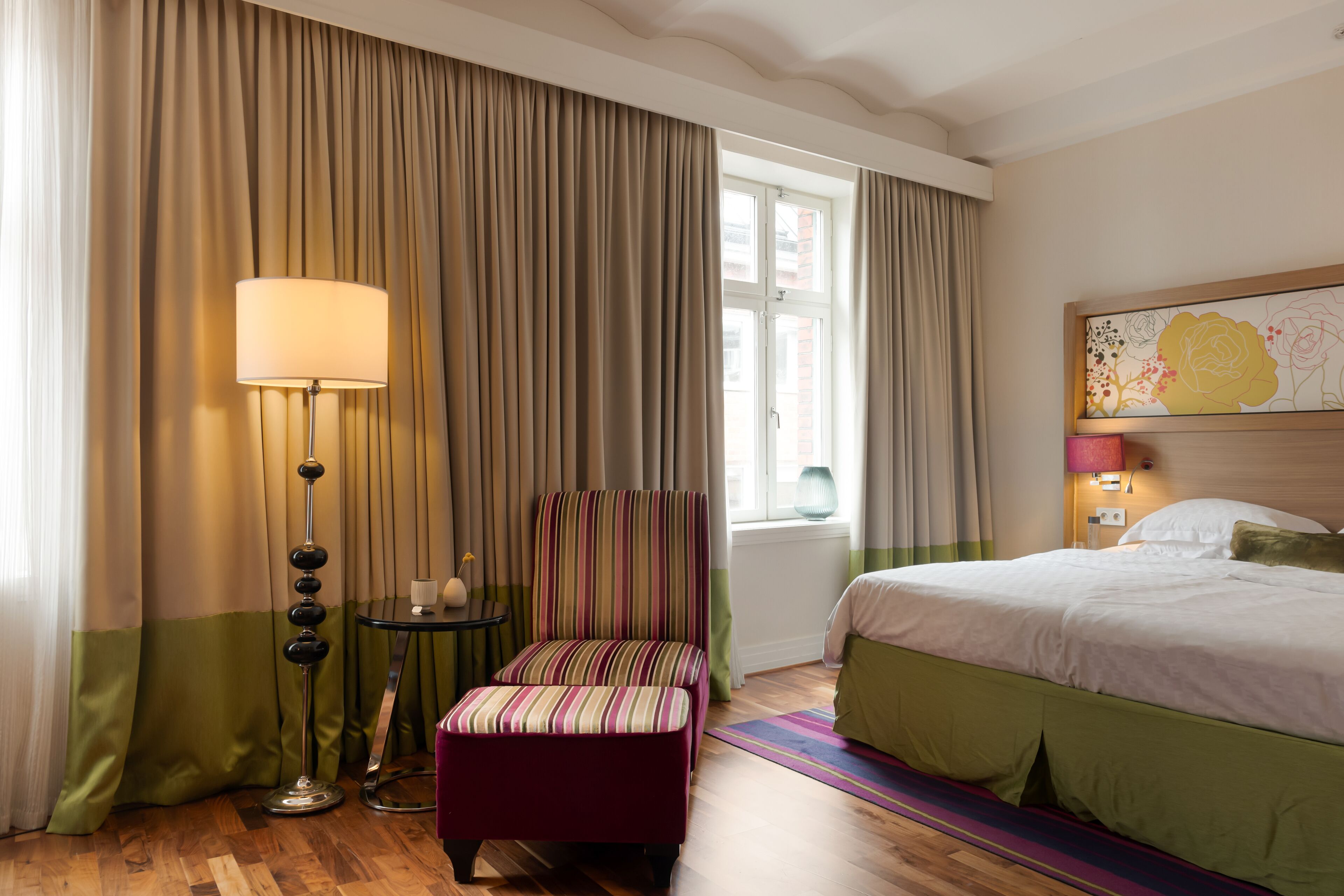Ett hotellrum med en säng, en stol, ett bord och en lampa.