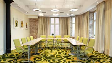 Un salón de conferencias con una larga mesa, sillas verdes y una alfombra estampada.