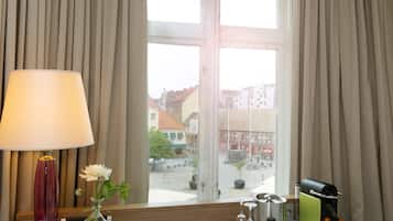 Quarto de hotel com uma escrivaninha, uma luminária, um vaso com flores e vista para prédios.