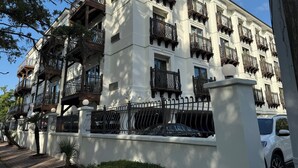 A multi-story building with balconies, a gated entrance, and a parked car.