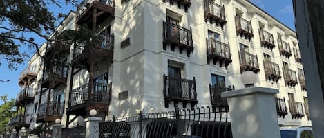 A multi-story building with balconies, a gated entrance, and a parked car.