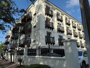 A multi-story building with balconies, a gated entrance, and a parked car.