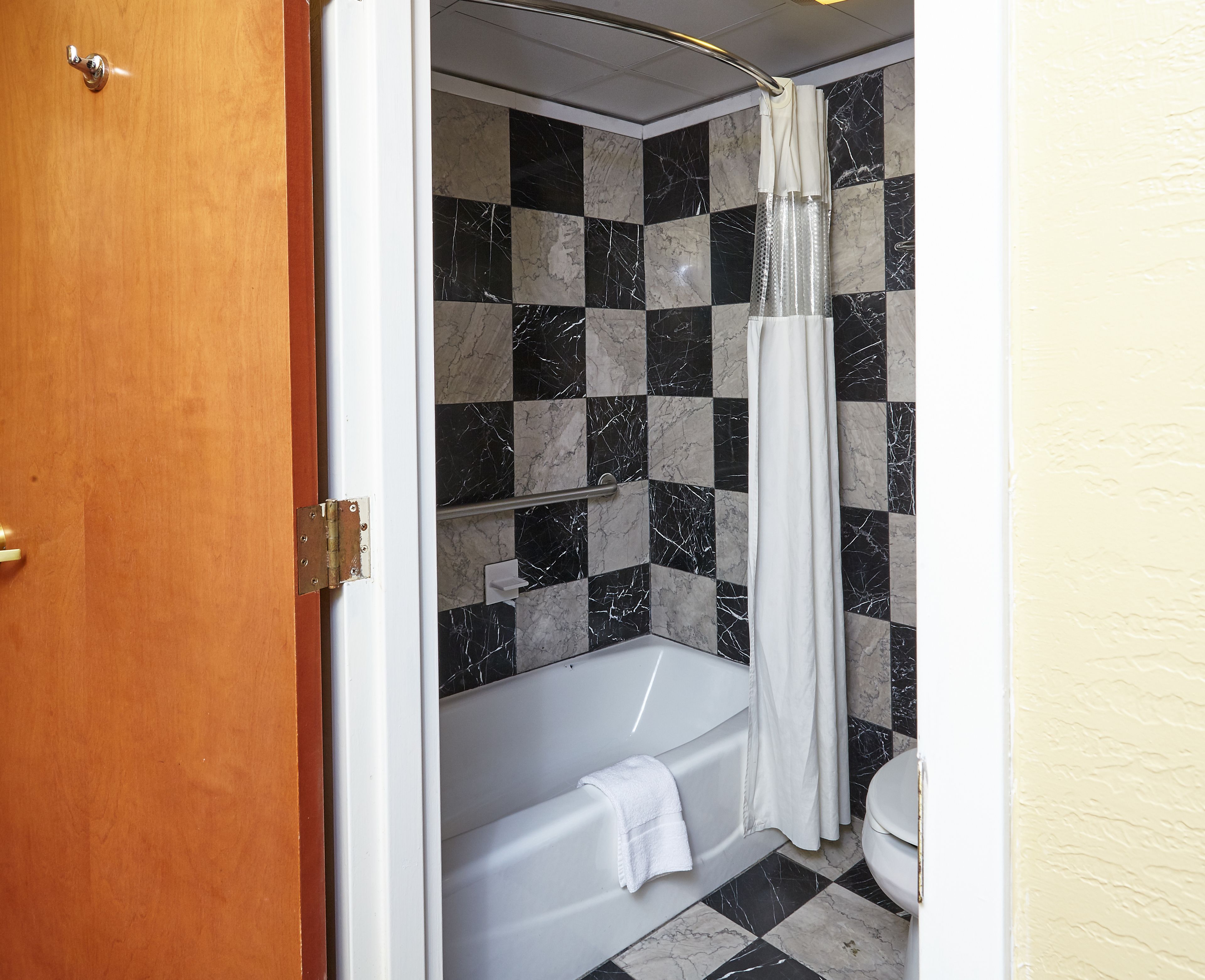 A bathroom with a checkered black and white tile wall, a white bathtub, and a white toilet.