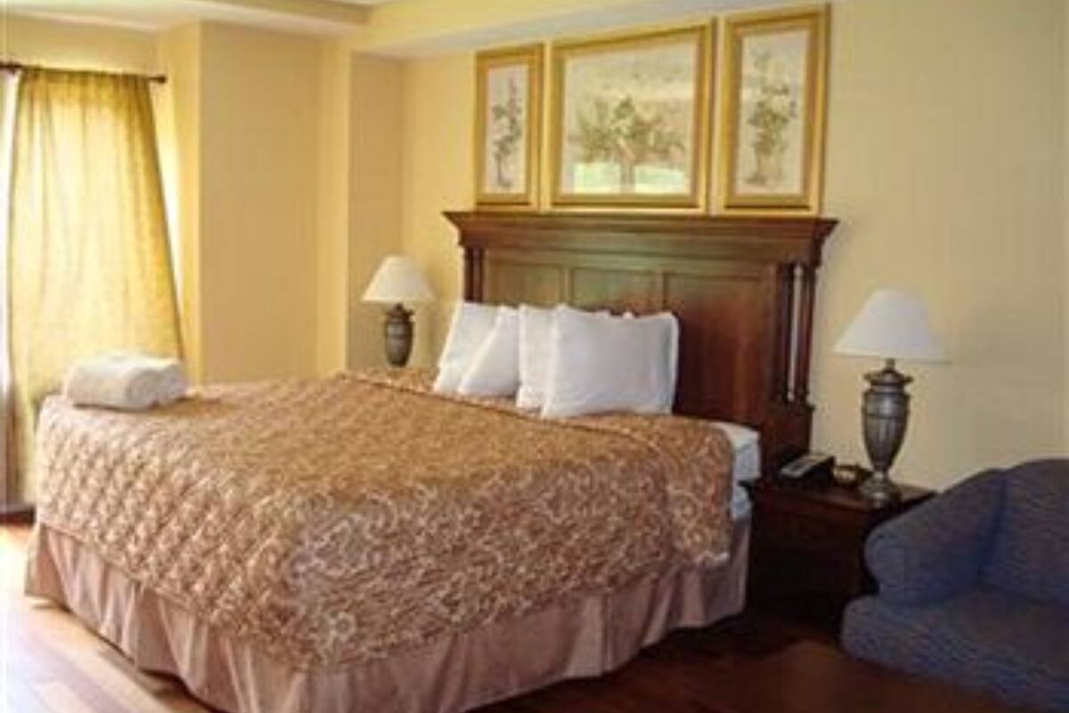 A hotel room with a large bed, two bedside lamps, a wooden headboard, and a framed picture above the bed.