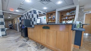 A reception area with a marble floor, a reception desk, a digital display, and a clock on the wall.
