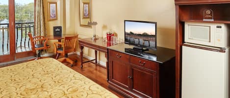 A hotel room with a bed, a desk with a television, a refrigerator, and a dining area with chairs and a table.