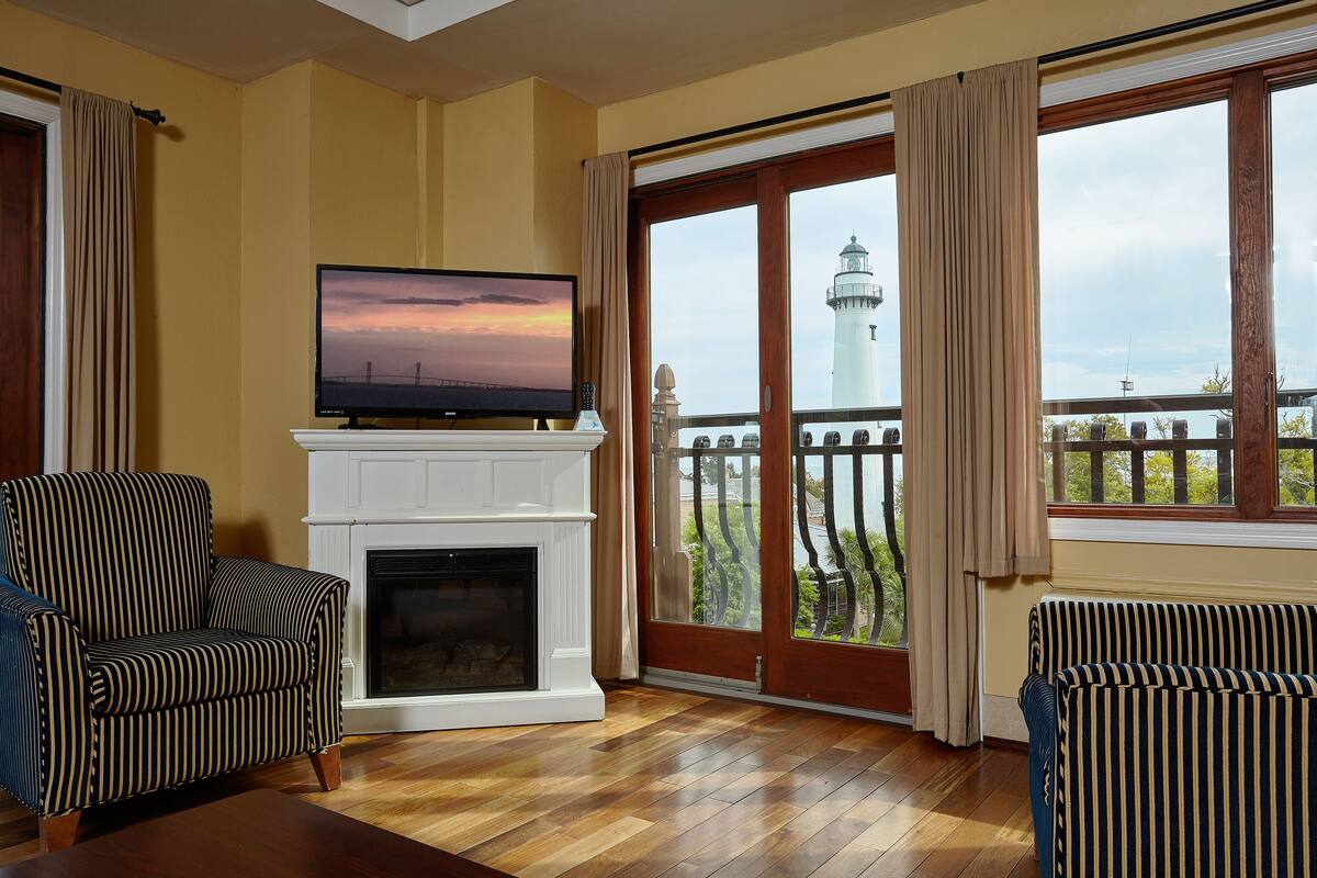 A living room with a fireplace, a television, and a view of a lighthouse through large windows.