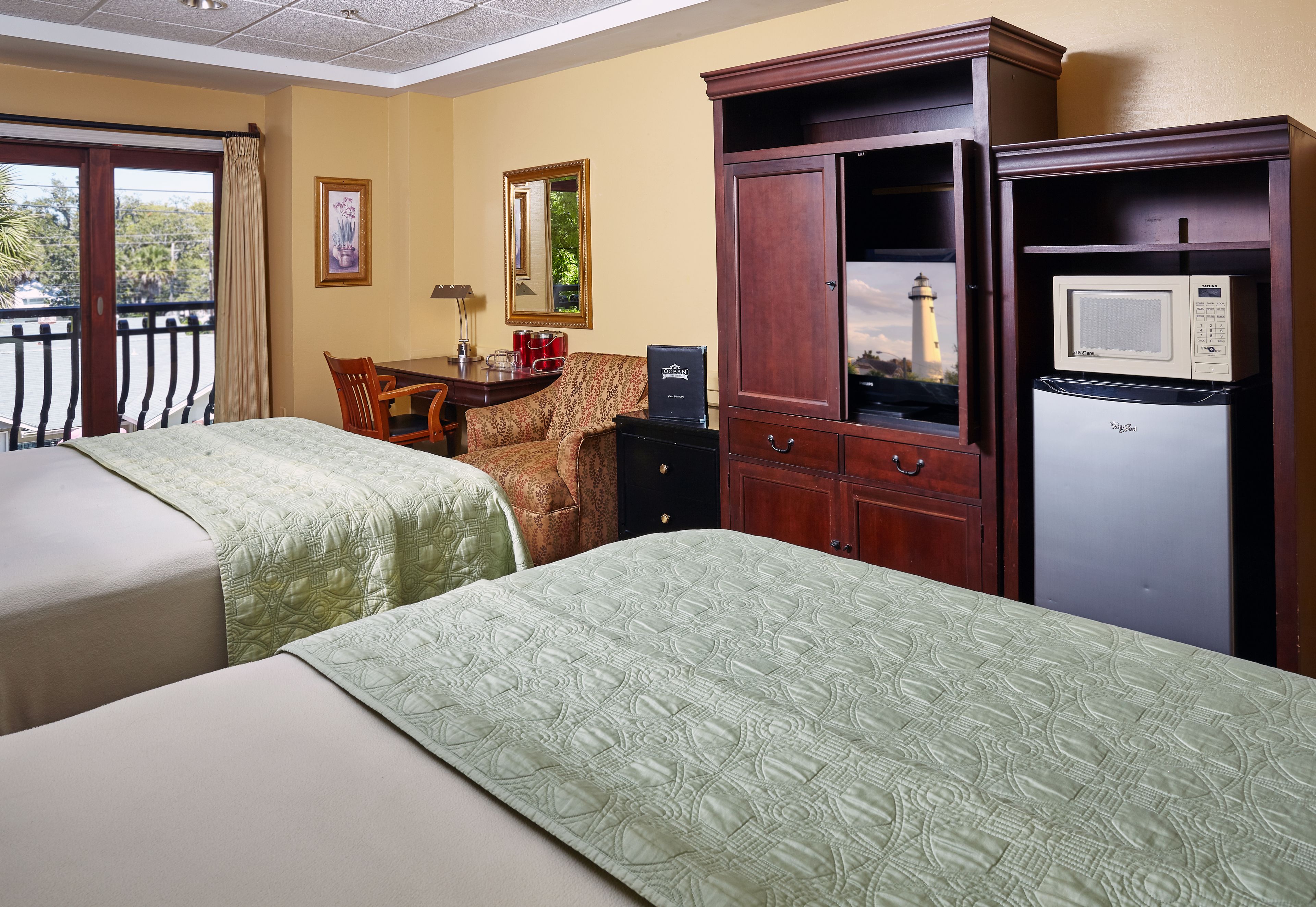 A hotel room with two beds, a desk, a chair, a cabinet, and a microwave.
